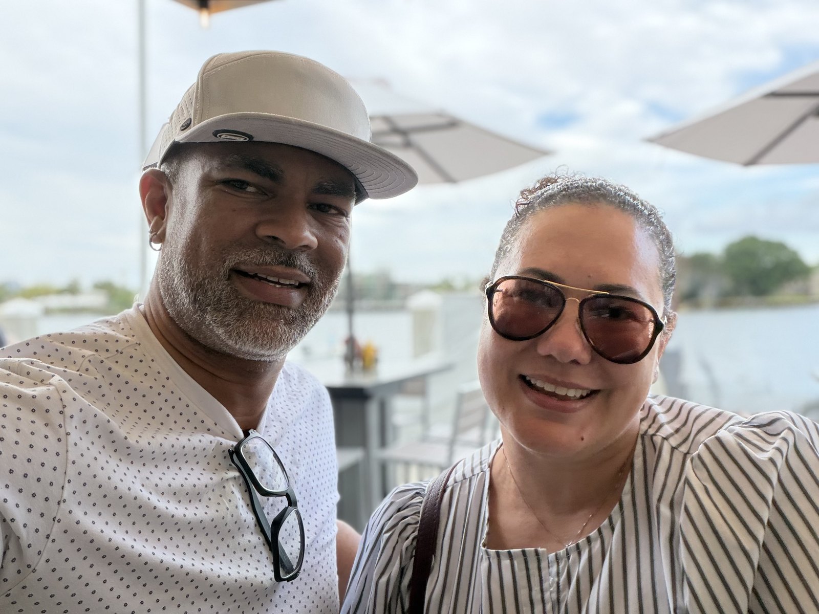 Félix and Gina Rivera-Mariani smiling at the camera on a waterfront patio under white umbrellas.
